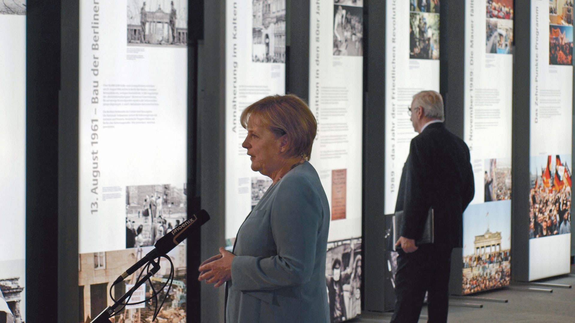 Angela Merkel hät eine Rede vor Ausstellungstafeln